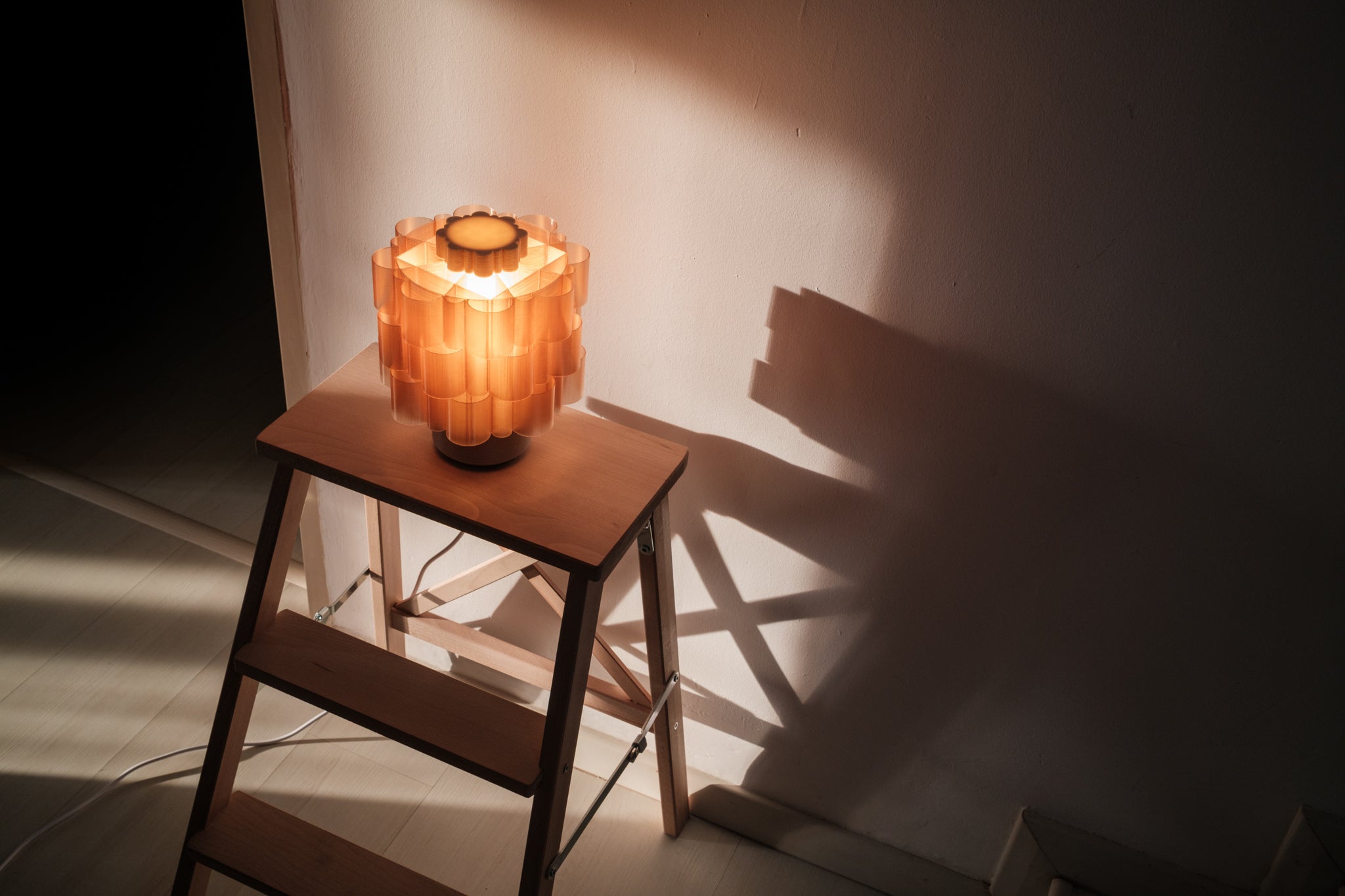 Decorative lamp on a small wooden stool casting shadows on a wall.