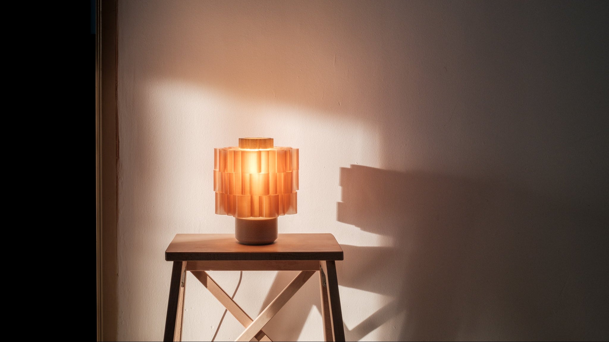 Table lamp with a warm glow on a wooden table against a plain wall.